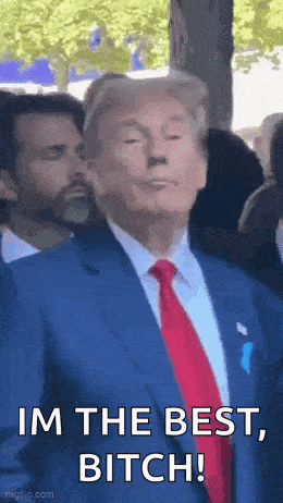 donald trump is wearing a suit and tie and making a funny face while standing in front of a crowd .