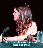 a woman is sitting at a table in front of a microphone talking to someone .