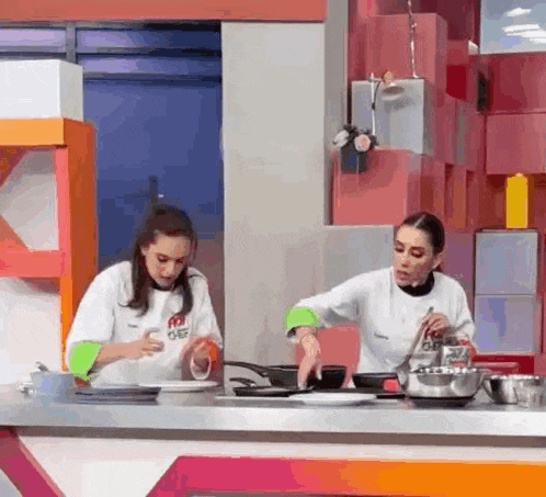 two women are standing at a counter in a kitchen cooking food .
