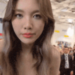 a woman with long brown hair is looking at the camera in a crowded room .