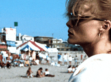 a woman wearing sunglasses stands on a beach