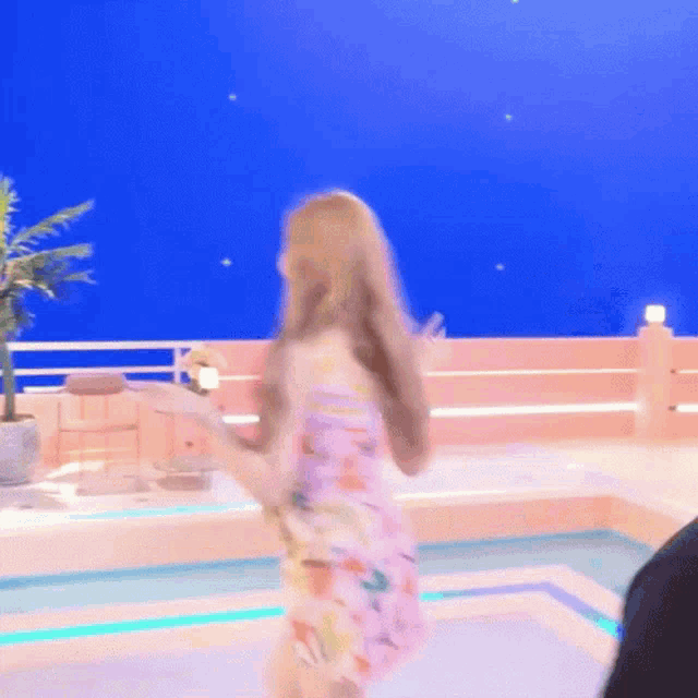 a woman in a pink dress is dancing in front of a pool
