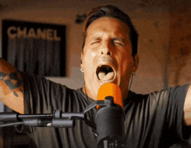 a man is singing into a microphone in front of a chanel sign