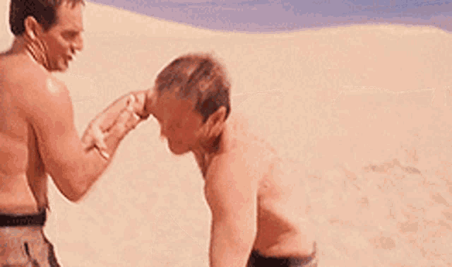 two men without shirts are fighting in the sand .