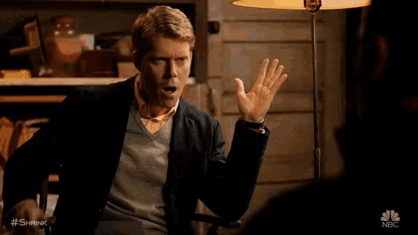 a man sitting in front of a lamp with his hands in the air and says wow