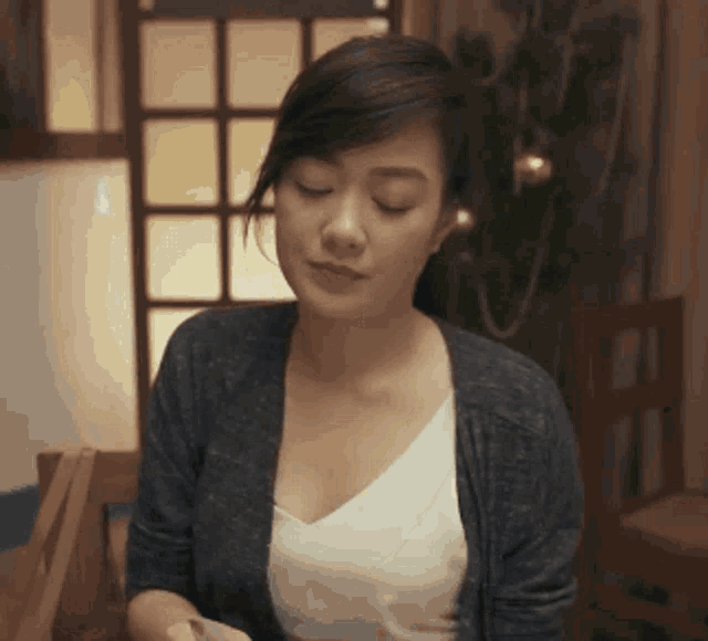 a woman is sitting at a table with her eyes closed and looking down