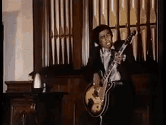 a man in a suit and tie is playing a guitar in front of an organ .