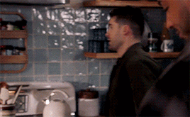 two men are standing in a kitchen with a white kettle