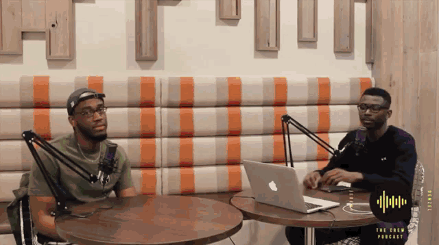 two men are sitting at a table with a laptop and a microphone in front of them with a logo that says the new podcast
