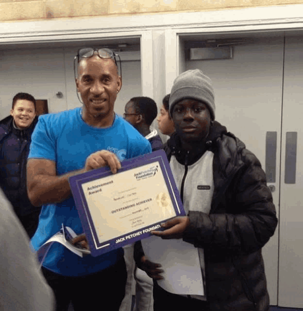 a man is holding a certificate that says achievement award on it