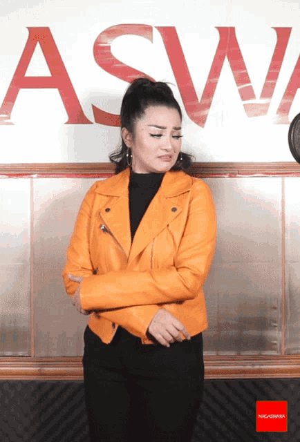 a woman in an orange leather jacket is standing in front of a sign that says asw