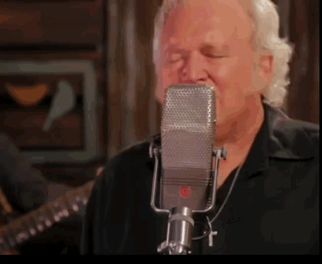 a man is singing into a microphone with a cross necklace around his neck
