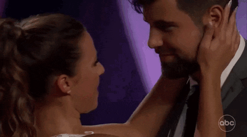 a man and woman are kissing in front of a purple background .