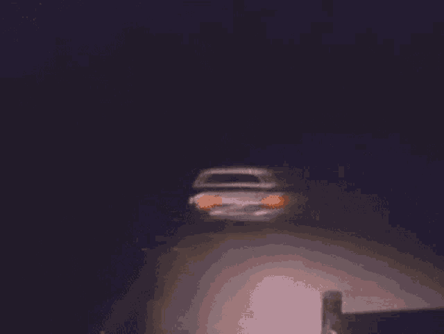 a car is driving down a dark road at night with its headlights on .