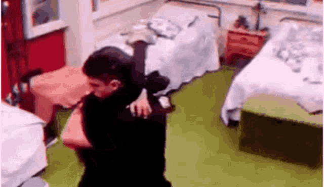 a man is carrying another man on his shoulders in a bedroom with two beds .