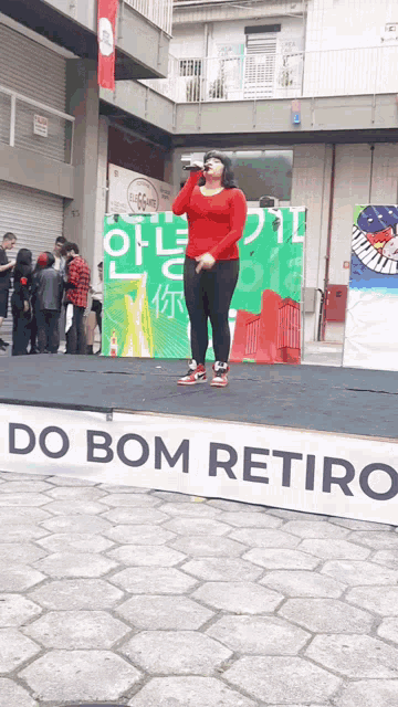 a woman stands on a stage with a sign that says do bom retiro