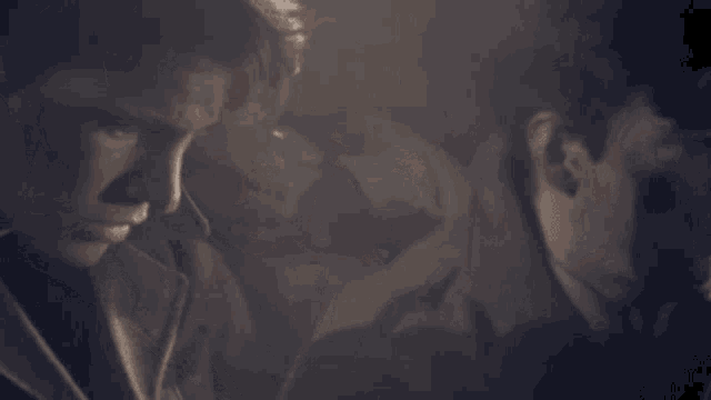 two men are standing next to each other in a dark room looking down at something .