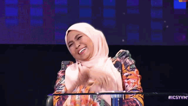a woman wearing a hijab is sitting at a table and laughing .