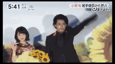 a man in a suit is holding a bouquet of sunflowers next to a woman in a red dress .