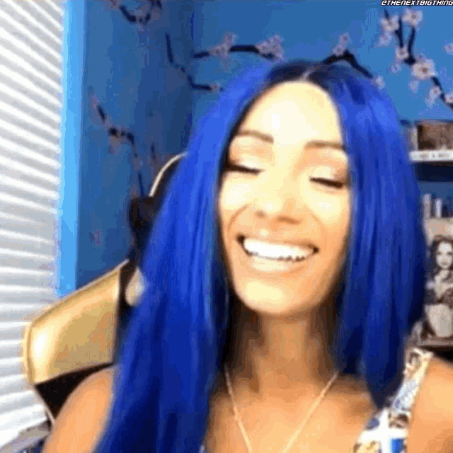 a woman with blue hair is smiling with her eyes closed in a room .