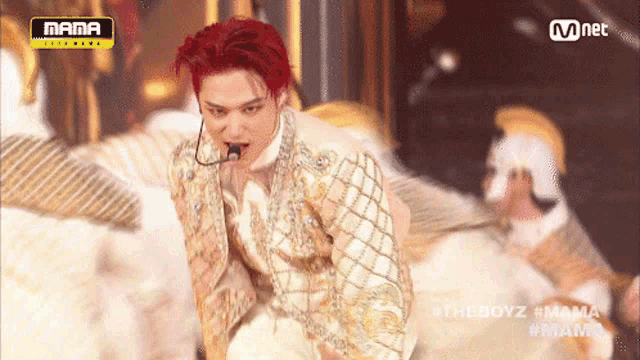 a man with red hair is singing into a microphone while wearing a white and gold suit