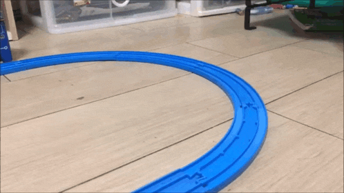 a toy train going around a blue track on a wooden floor