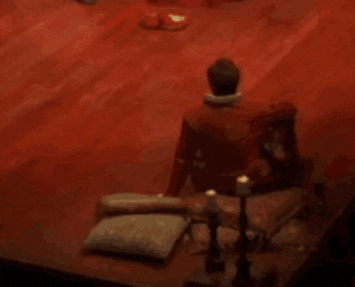 a man in a red jacket is sitting on a red floor with candles and pillows .