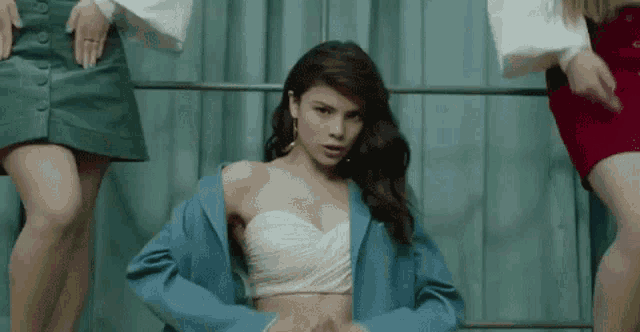 a woman in a blue jacket and a pink crop top is dancing with two other women in skirts .