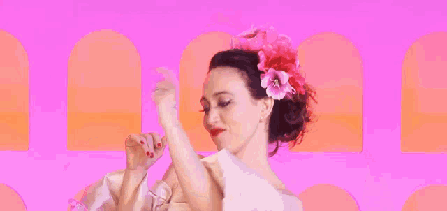 a woman with a flower in her hair is dancing in front of a pink and orange background .