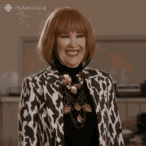 a woman wearing a leopard print jacket and a gold necklace smiles for the camera