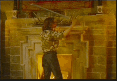 a man in a floral shirt is holding a sword in front of a fireplace
