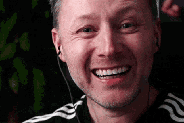 a man wearing headphones and a black and white adidas shirt smiles
