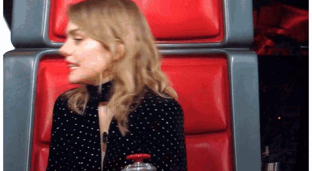 a woman sits in a red chair with a bottle of water in her hand