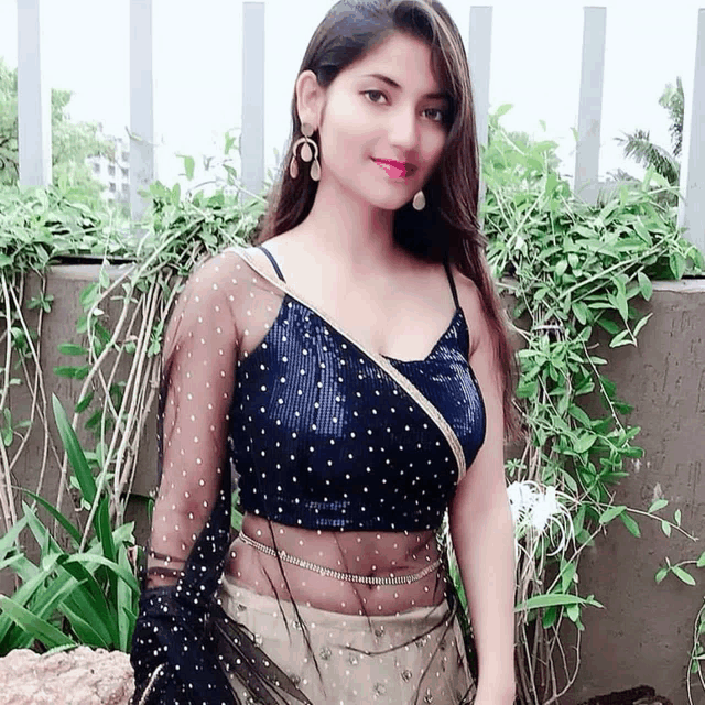 a woman wearing a black top with gold polka dots is standing in front of a fence