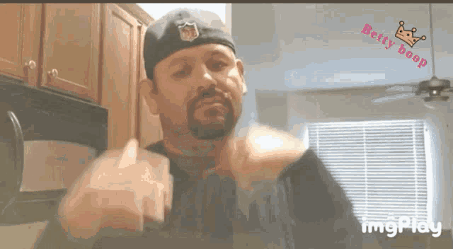 a man with a beard wearing a nfl hat is giving the middle finger in a kitchen