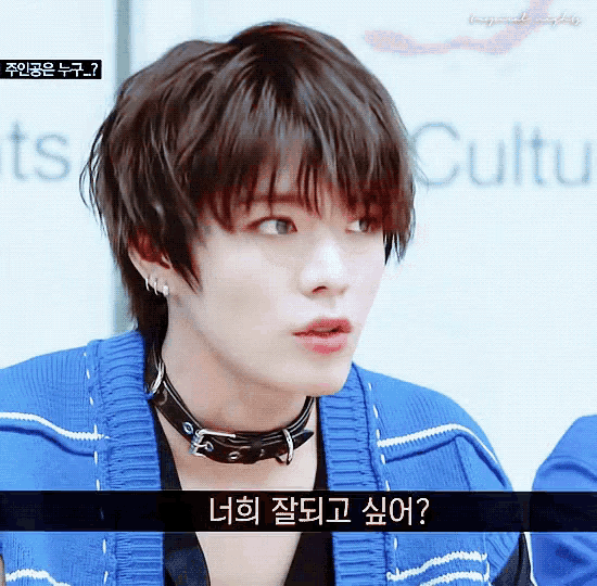 a young man wearing a blue sweater and a choker looks at the camera