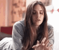 a woman is laying on her stomach on a bed with her eyes closed and her hands up .