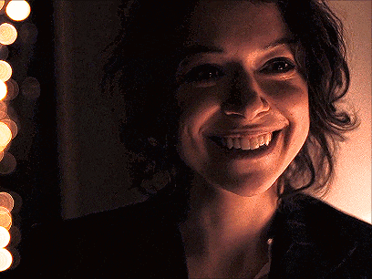 a woman is smiling in a dark room with a string of lights in the background