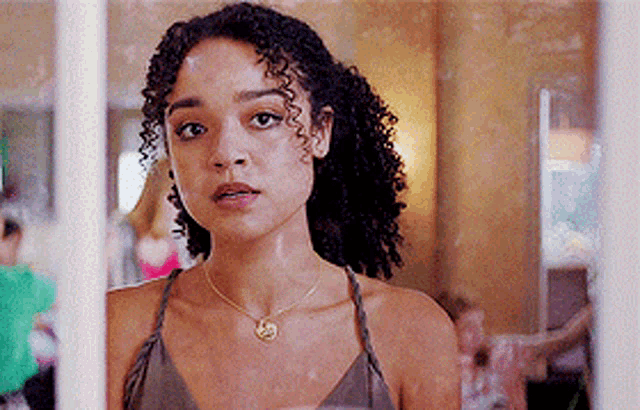 a woman with curly hair is standing in front of a window looking out .