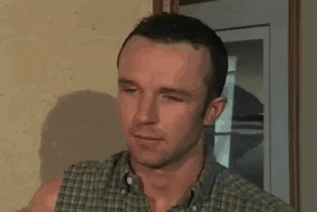 a man in a plaid shirt is standing in front of a door and looking at the camera .