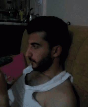 a man with a beard wearing a white tank top sits on a chair