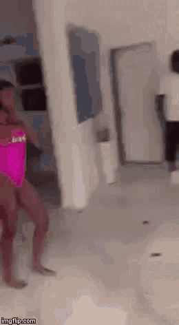 a woman in a pink bikini is dancing in a living room while a man looks on .
