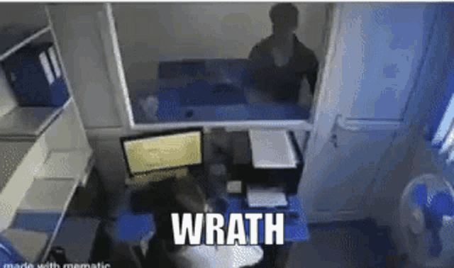 a person is sitting at a desk in front of a computer with the word wrath written on the bottom .