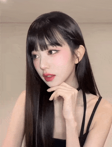 a woman with long black hair and red lipstick holds her hand to her chin