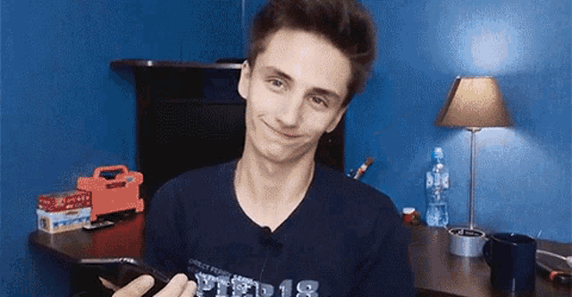 a young man is smiling while holding a cell phone in front of him .