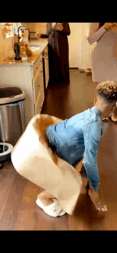 a man in a denim shirt is kneeling on the floor with a pillow on his back .