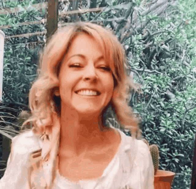 a woman is smiling and looking at the camera while standing in front of trees .