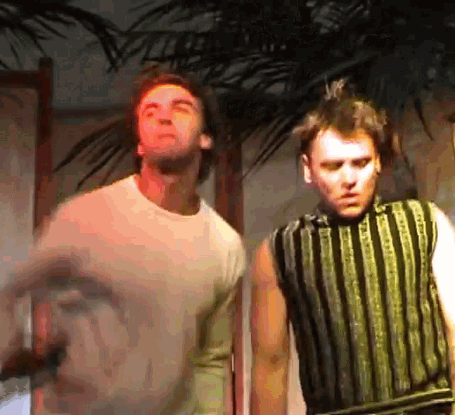 two men standing next to each other with one wearing a striped vest