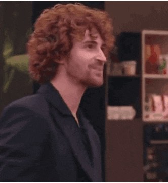 a man with curly red hair and a beard is wearing a black suit and smiling .
