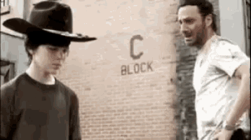 a man in a cowboy hat is standing next to a man in a white shirt .